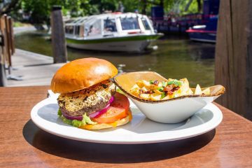 burger and salad on a white plate. In the background is a river and a white boat.
