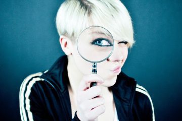 blonde woman holding magnifying glass in front of her eye