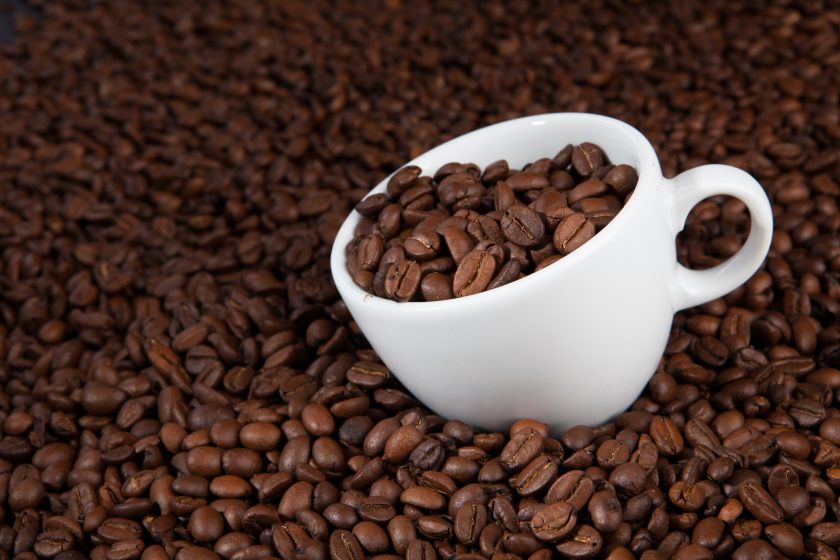 white cup filled with coffee beans, sitting in a pile of coffee beans