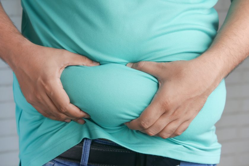 close up of obese person wearing blue top, grabbing stomach