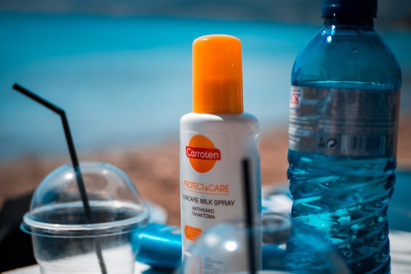 white and orange bottle of sunscreen next to a bottle of water and plastic cup with a straw